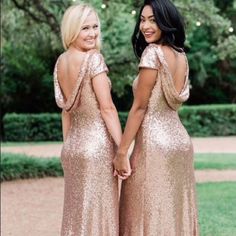 two women in gold sequin dresses holding hands