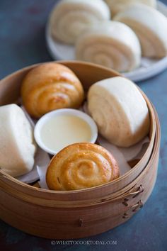 some food is in a wooden bowl on a table next to another plate with rolls