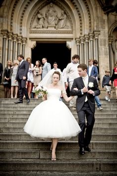 a bride and groom walking down the stairs in front of an old building with people standing around