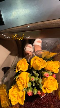 a bouquet of yellow roses sitting on top of a table next to someone's feet