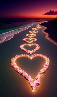 a long line of flowers in the shape of a heart on a beach at sunset