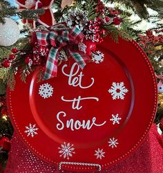 a red plate with let it snow written on the side in front of a christmas tree