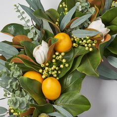 an arrangement of oranges and greenery on a white wall with flowers in the center