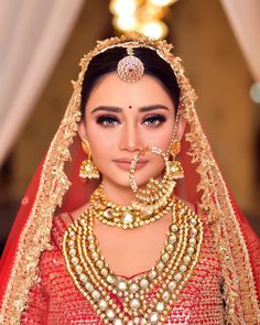 a woman in a red and gold bridal outfit with jewelry on her neck, nose ring