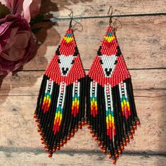 a pair of colorful beaded earrings sitting on top of a wooden table next to flowers