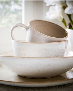 a stack of white dishes sitting on top of a table next to a vase with flowers in it