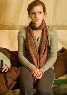 a young woman sitting on top of a bed wearing a plaid scarf and brown pants