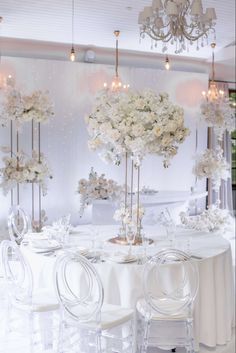 there are many chairs around the table with flowers on it and chandeliers hanging from the ceiling