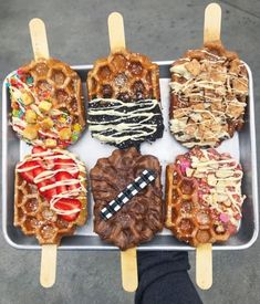 four waffles with different toppings on them sitting in a tray next to a person's hand