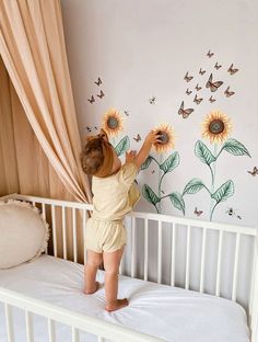 a small child standing on top of a crib next to a wall with sunflowers