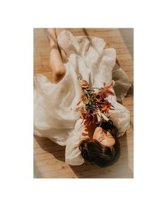 a woman laying on the ground with flowers in her hair and wearing a white dress