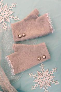 two gray mittens sitting on top of a table covered in snowflakes and beads