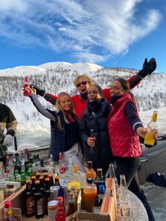 three women standing in front of a table full of drinks and bottles with their arms up