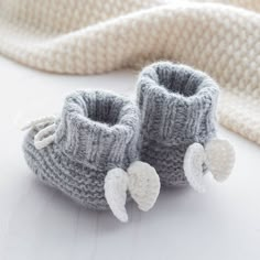 a pair of knitted baby booties with angel wings on the toes, sitting next to a white blanket