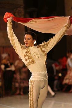 a man in white and gold outfit holding up a red scarf over his head while standing on a stage