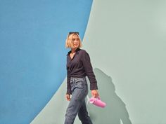 a woman holding a pink object in her right hand and walking past a blue and white wall