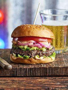 a hamburger sitting on top of a wooden cutting board next to a glass of beer