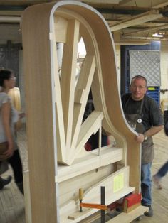 a man standing next to a large wooden structure in a room with people walking around