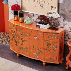 an orange cabinet with flowers and birds painted on the doors is in front of a wall