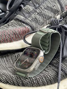 an apple watch resting on top of a pair of running shoes with the strap down