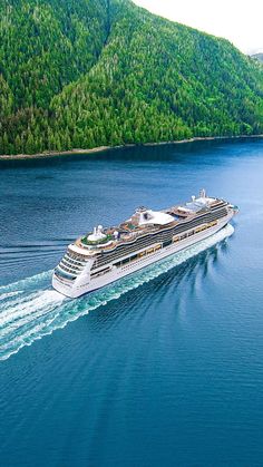 a cruise ship sailing in the middle of water near mountains and forest on either side