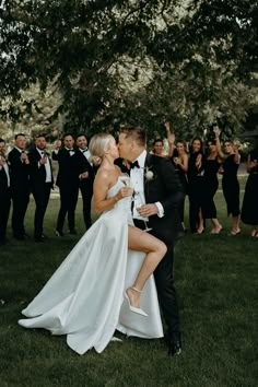 a bride and groom kissing in front of a large group of people wearing tuxedos