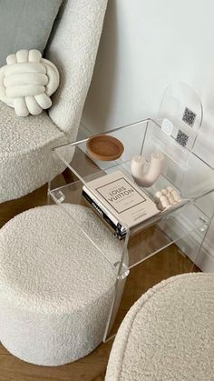 a white chair and ottoman with a book on the table next to it, in front of a wall