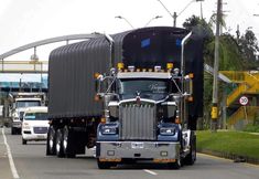 a semi truck driving down the road with other cars behind it and an overpass in the background