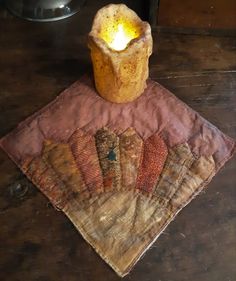 a candle sitting on top of a table next to an old piece of cloth with quilts