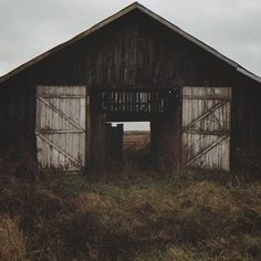 an old barn sits in the middle of a field