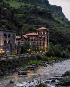 a river running through a lush green hillside next to a tall building on top of a hill