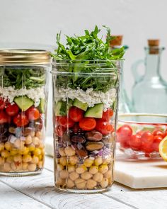 two mason jars filled with different types of vegetables and veggies on a table