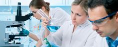 four people in lab coats and gloves looking at something on a table with microscopes