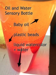 an orange and red liquid in a glass with labels on the bottom, labeled baby oil, plastic beads, liquid water, and water