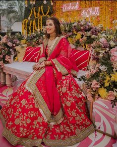 a woman in a red and gold bridal gown sitting on a bench surrounded by flowers