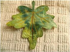 a green leaf with yellow thread on it sitting on top of a white cloth covered surface