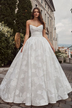 a woman in a white wedding dress standing on a cobblestone street