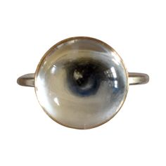 Lover's Eye ring with a round oil painting encased in gold plate over sterling with a quartz crystal cabochon which gives a magical magnifying effect, measuring 1/2"; ring size 5.5. THE HISTORY: Lover's Eyes were a jewelry trend c.1785-1830 of brooches set with tiny watercolor portraits on ivory. Since they were cropped to eyes, they were in many ways more direct and intimate than traditional miniature portraits; but also because they were just eyes, they were often used as daring public testimonies of clandestine love affairs with mystery lovers. THE SETTINGS: This piece is part of the collection of contemporary minimalist settings which juxtapose this historical jewelry tradition with clean, modern lines for a subtle effect that's easy to wear. Gold Moonstone Cabochon Ring, Gold Moonstone Ring Collectible, Spiritual Gold Moonstone Cabochon Ring, Gold Cabochon Moonstone Ring Collectible, Brass Dome Ring For Anniversary, Gold Cabochon Dome Ring, Spiritual Yellow Gold Round Crystal Ring, Gold Dome Ring With Cabochon, Mystical Round Cabochon Jewelry