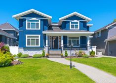 a blue house with white trim and two story houses in the front yard on a sunny day