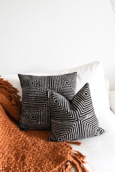 two black and white pillows sitting on top of a bed next to an orange blanket