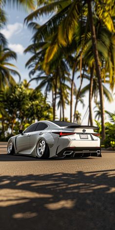 a silver sports car driving down a street next to palm trees and tall, leafy trees