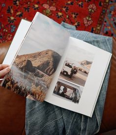 a person sitting on a couch holding an open book in their hand and looking at the photo