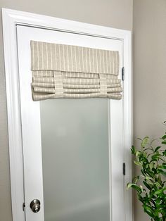 a white door with a window covering over it and a potted plant next to it