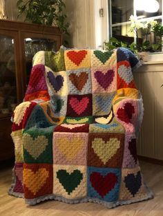 a crocheted blanket with hearts on it is sitting in front of a window