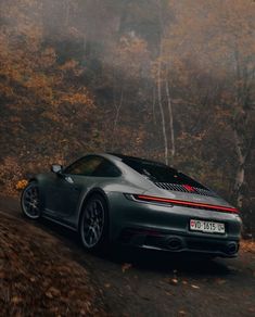 a grey sports car driving down a road in the woods