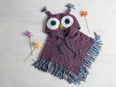 an owl scarf with crochet fringes and flowers on a white table next to it