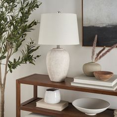 a white vase sitting on top of a wooden table next to a lamp and bowl