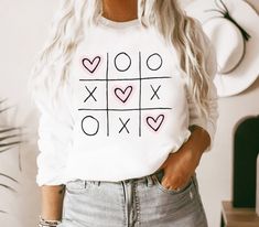 a woman wearing a white shirt with hearts and crosses on the front that says xoxo