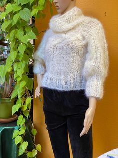 a mannequin wearing a white sweater and black pants next to a potted plant