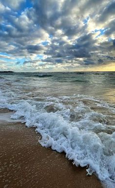 the waves are coming in to the beach and it is very cloudy sky over the water